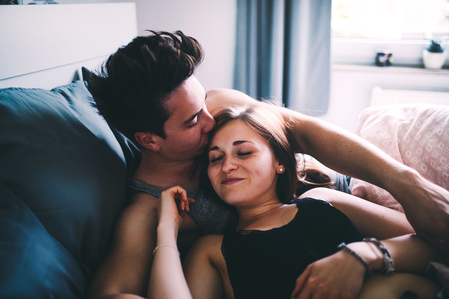 Casal na cama, homem está beijando a cabeça da mulher