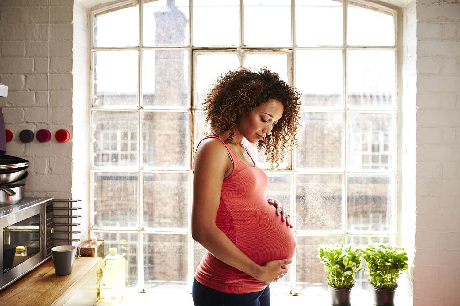 Uma mulher grávida em pé em uma cozinha segurando seu estômago